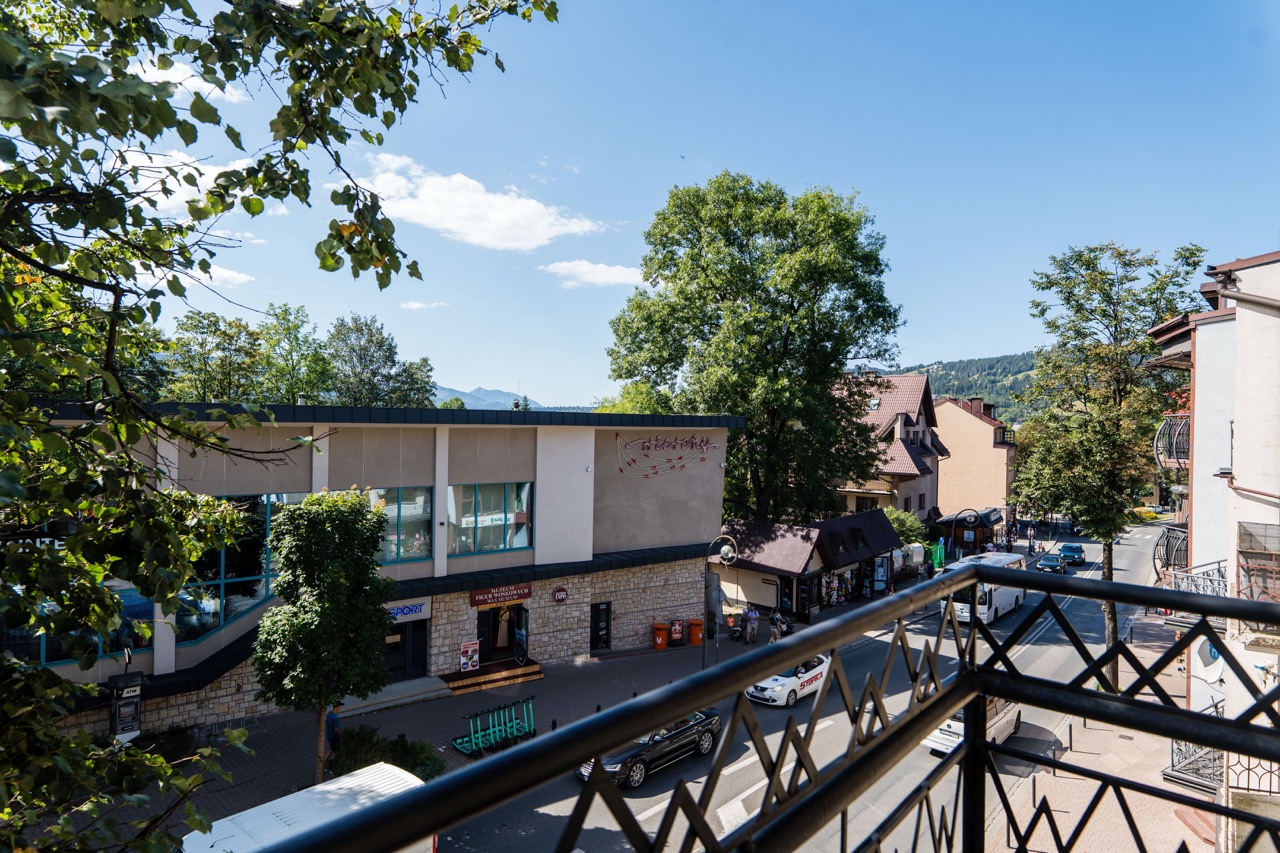 Widok z balkonu apartamentu w Zakopanem, z drzewami i ulicą w tle, idealny do relaksu.