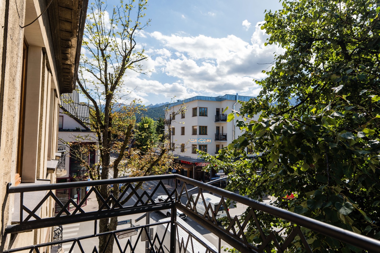 Widok z balkonu apartamentu w Zakopanem, z drzewami i budynkami w tle, idealny na relaksujący wypoczynek.