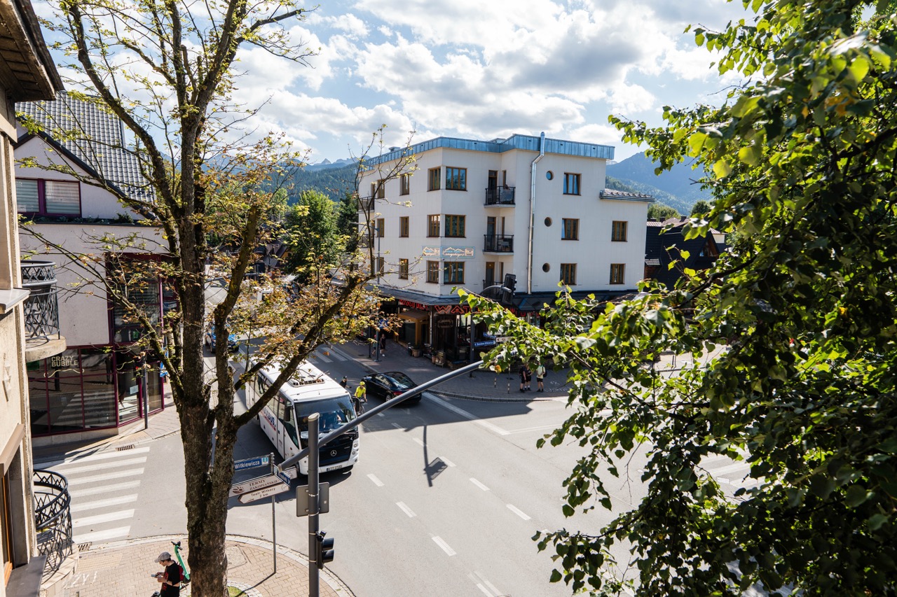 Widok z okna apartamentu w Zakopanem na ulicę z drzewami i budynkami w tle.