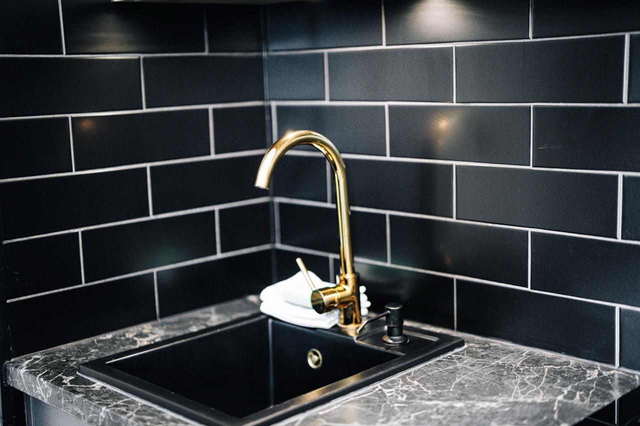 Elegancka zlew w kuchni apartamentu w Zakopanem, z czarną płytką i złotą armaturą.