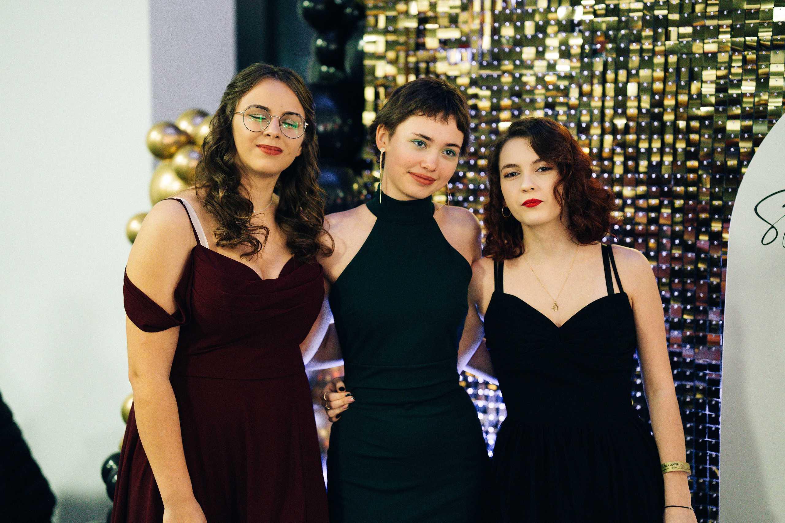 Trzy młode kobiety w eleganckich sukienkach pozują razem na studniówce w Hotelu Dana w Szczecinie.