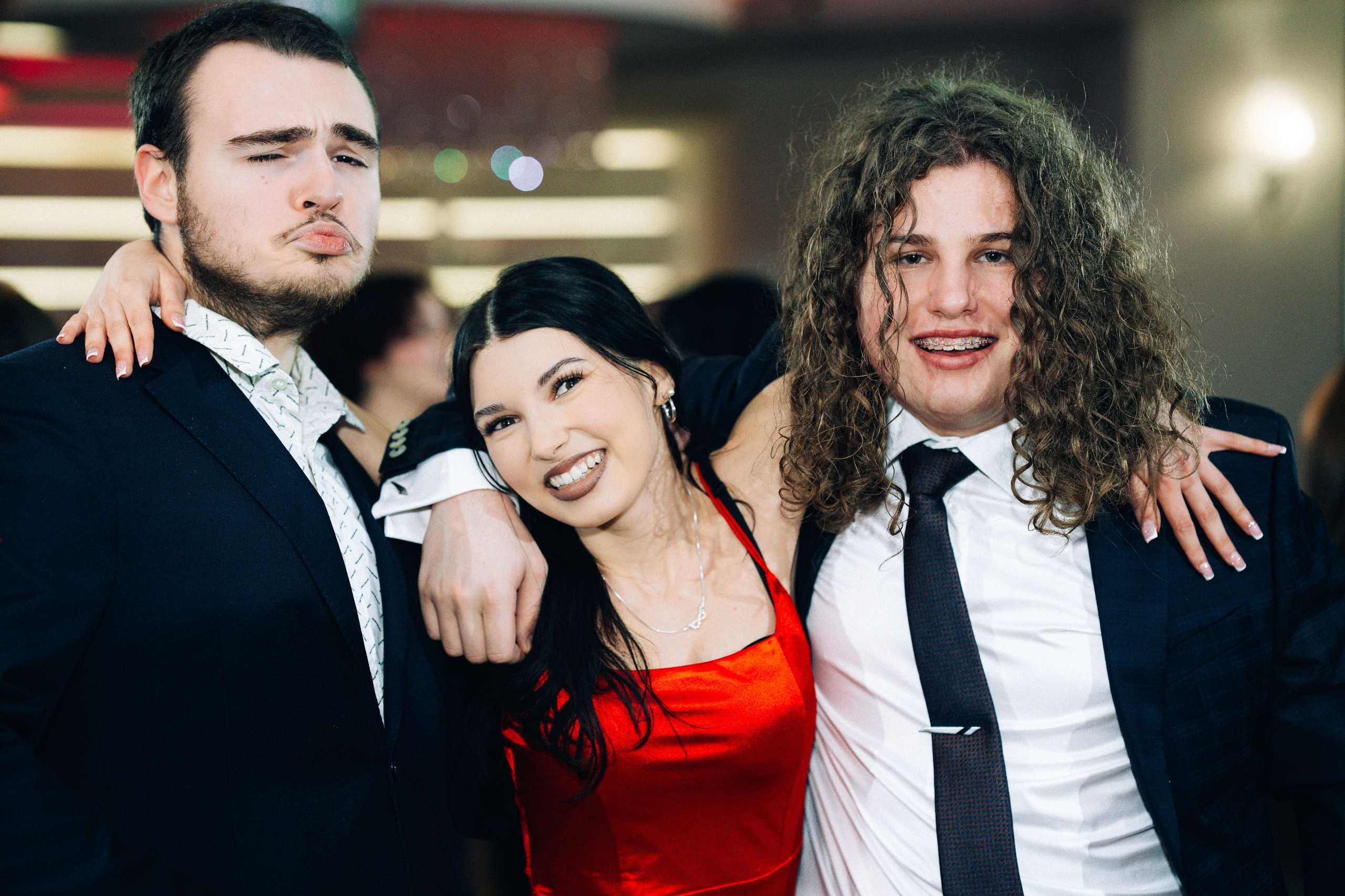 Trzy młode osoby w eleganckich strojach pozują razem na studniówce.