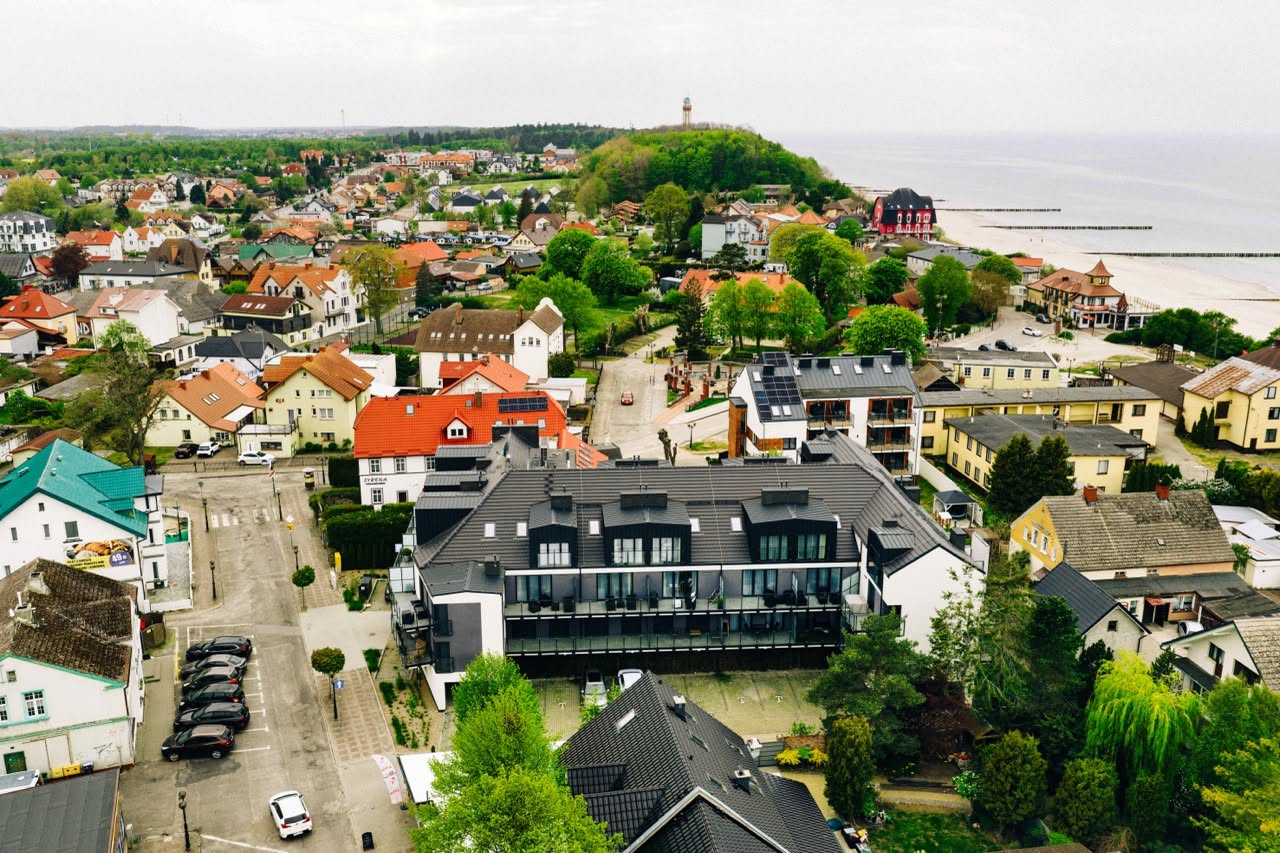 Fotografia apartamentu w Niechorzu — widok na nowoczesny budynek otoczony zielenią i nadmorskim krajobrazem.